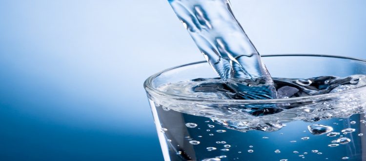 Pouring water into glass on blue background